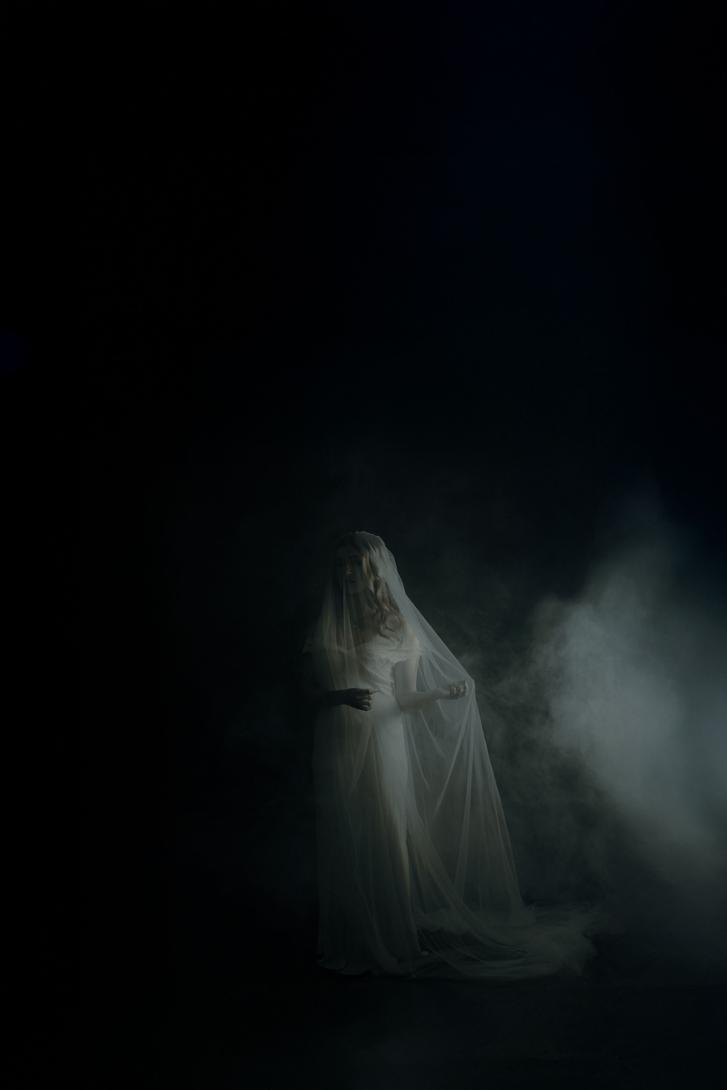 A ghostly figure in white fabric emerges from dark shadows creating an eerie supernatural atmosphere.
