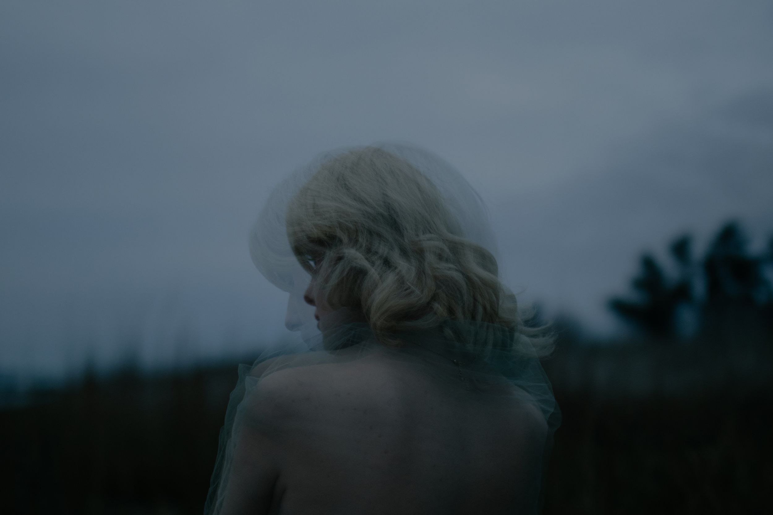 A dark silhouette of a person walking along a misty path through a moody forest landscape at dusk.
