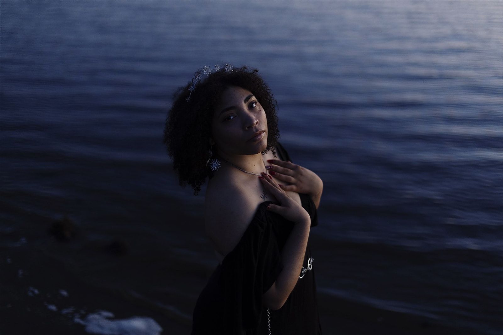 A silhouetted figure with curly hair gazes upward against a dark blue water background at dusk.