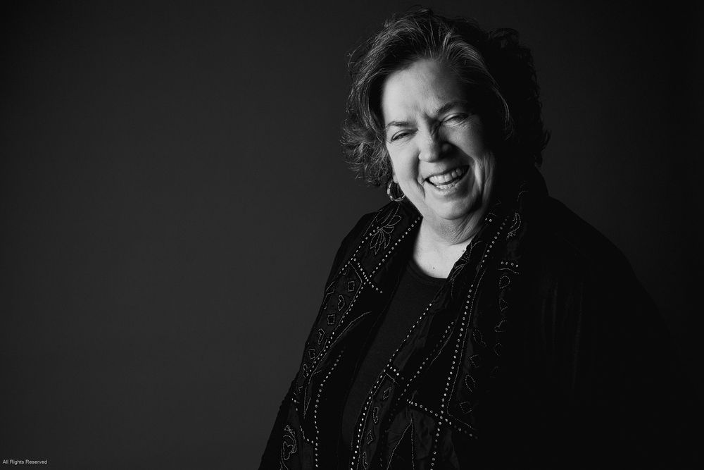 Black and white portrait of someone laughing expressively while wearing a dark sweater against a dark background.