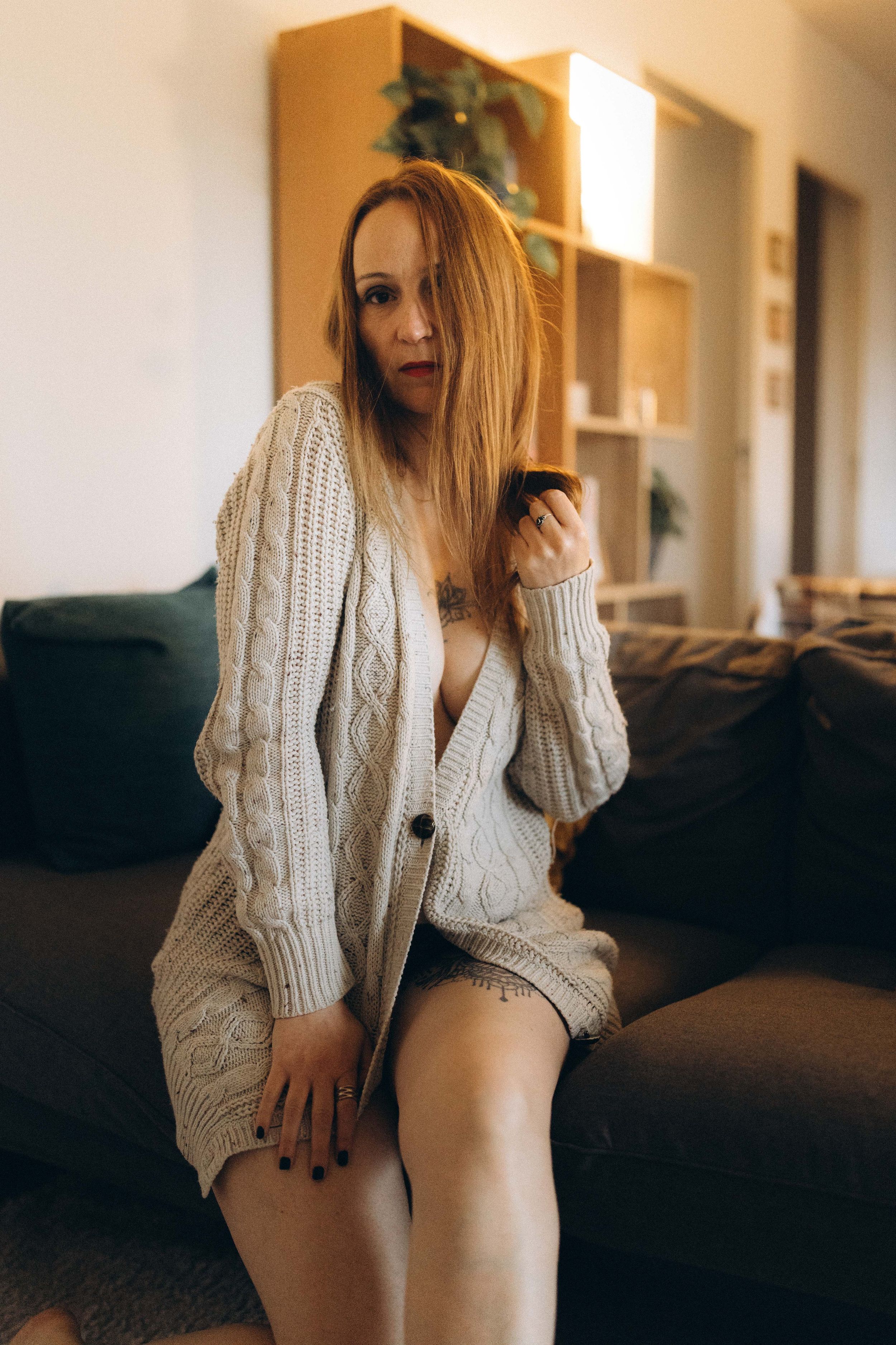 Person wearing a cozy white knit sweater lounges on a dark sofa in moody indoor lighting.
