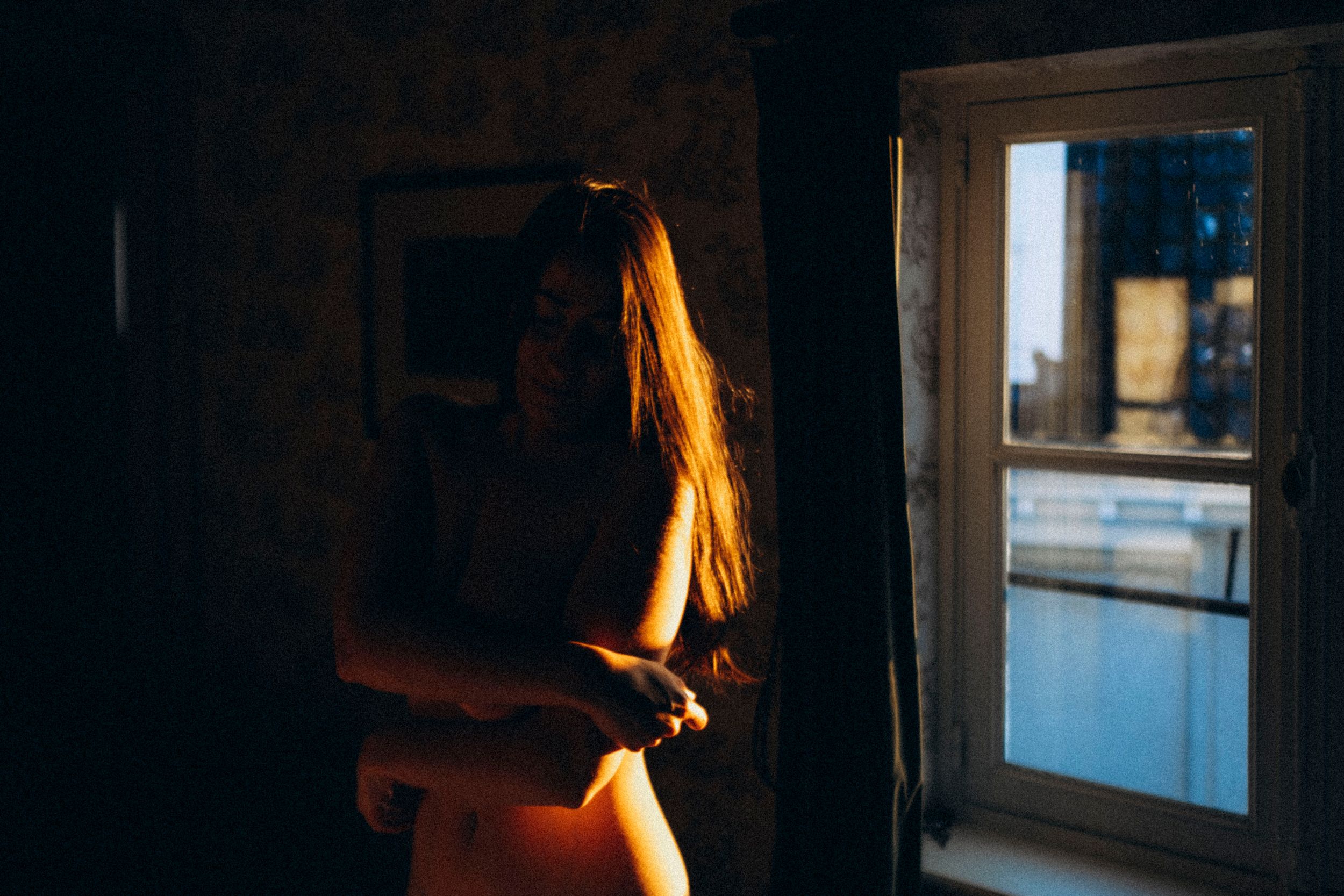 A silhouetted figure sits in contemplative solitude by a window with soft natural light streaming in.