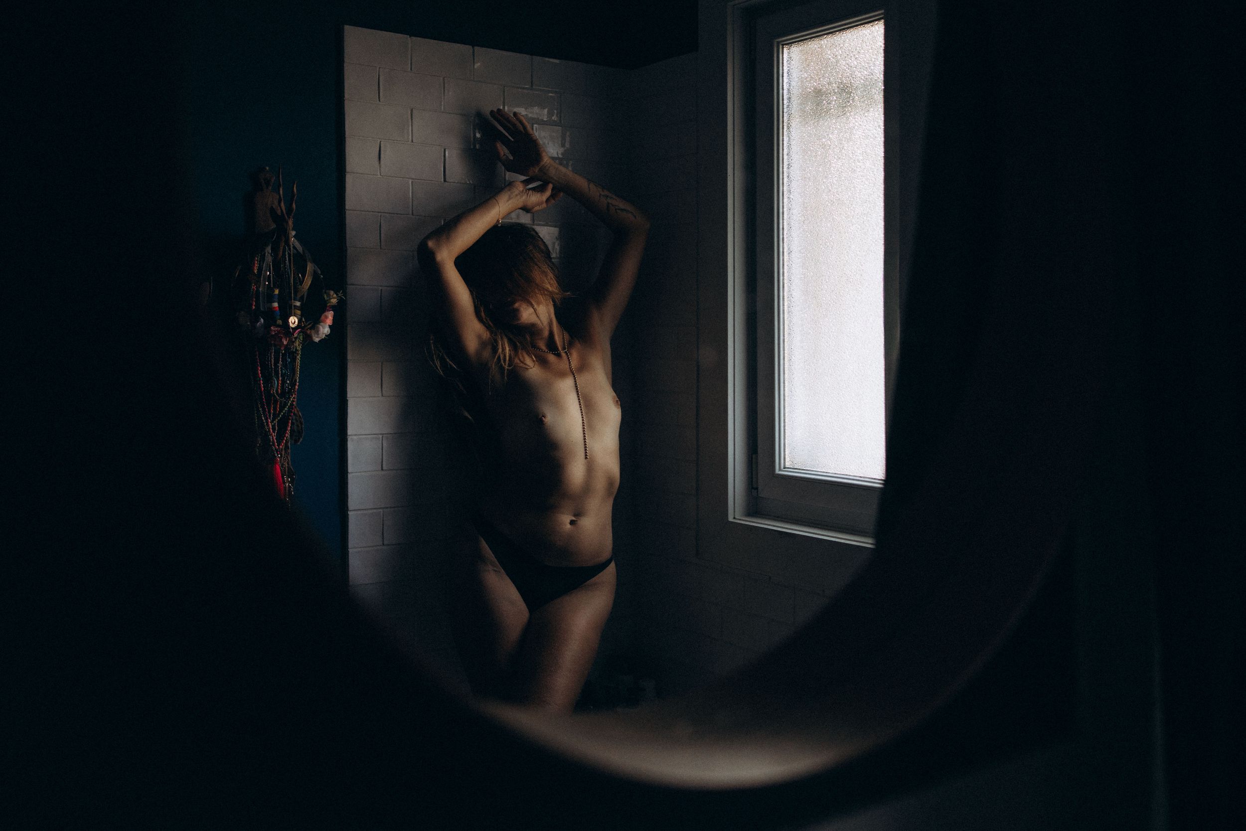 Artistic black and white portrait of a figure silhouetted against a bright window in moody lighting.