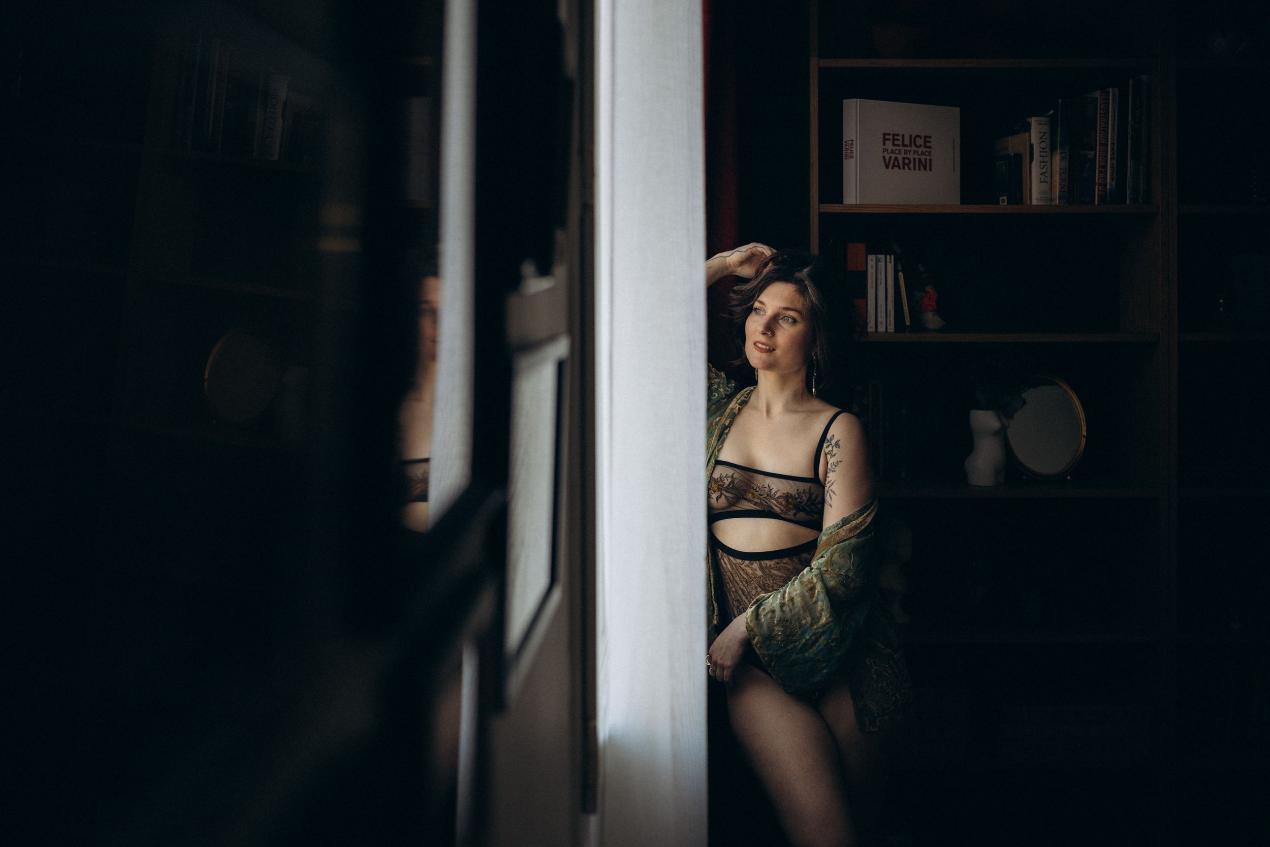 A moody black and white portrait photo of someone in lingerie against a dark background with dramatic lighting.