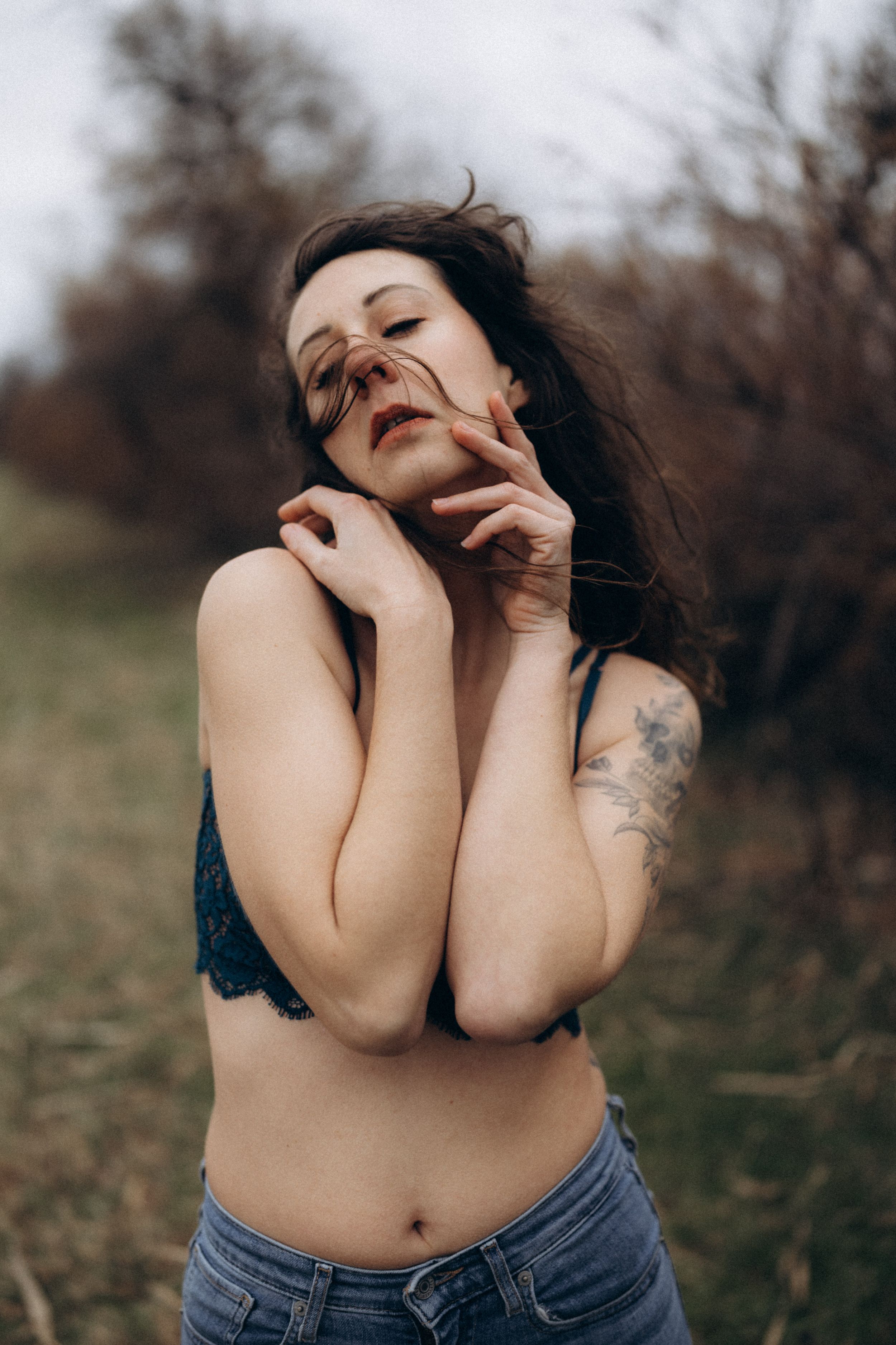 Person in denim jeans poses outdoors with expressive body movements against a natural backdrop.