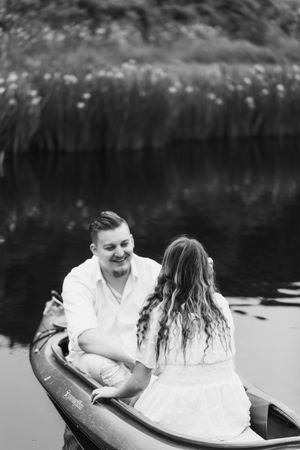 A romantic couple in white clothing share an intimate moment while sitting in a canoe on a tranquil lake.