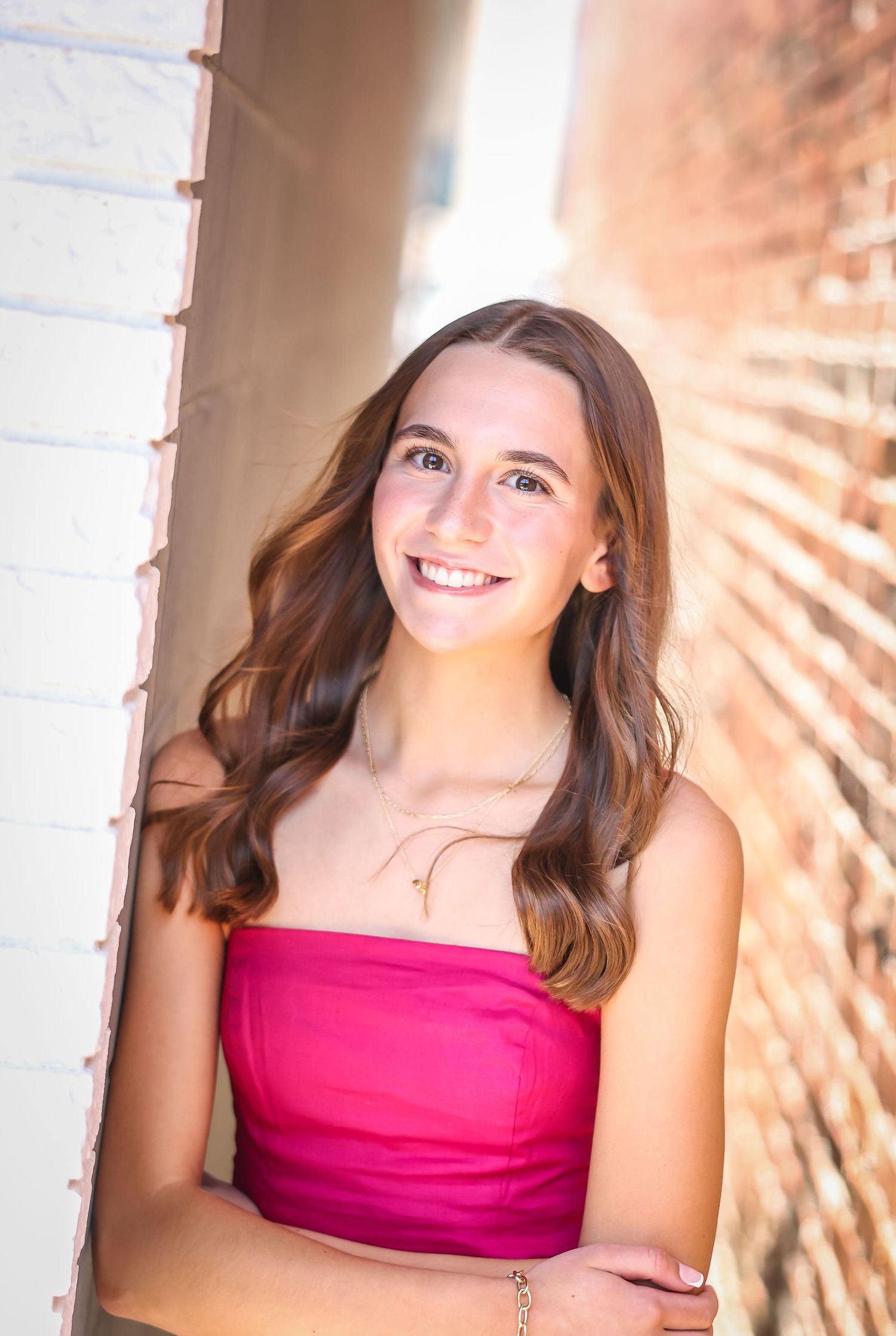 Portrait of a young woman in a pink dress smiling warmly in natural lighting.