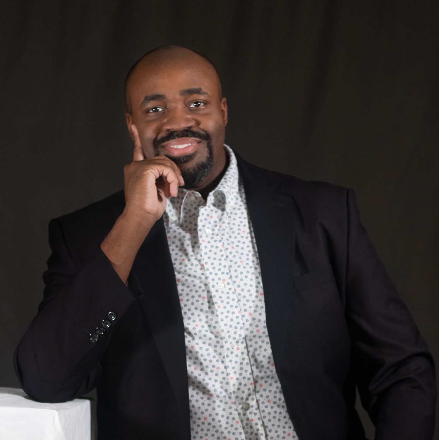 Professional headshot portraits in black suit and polka dot shirt against dark background showing different expressions.