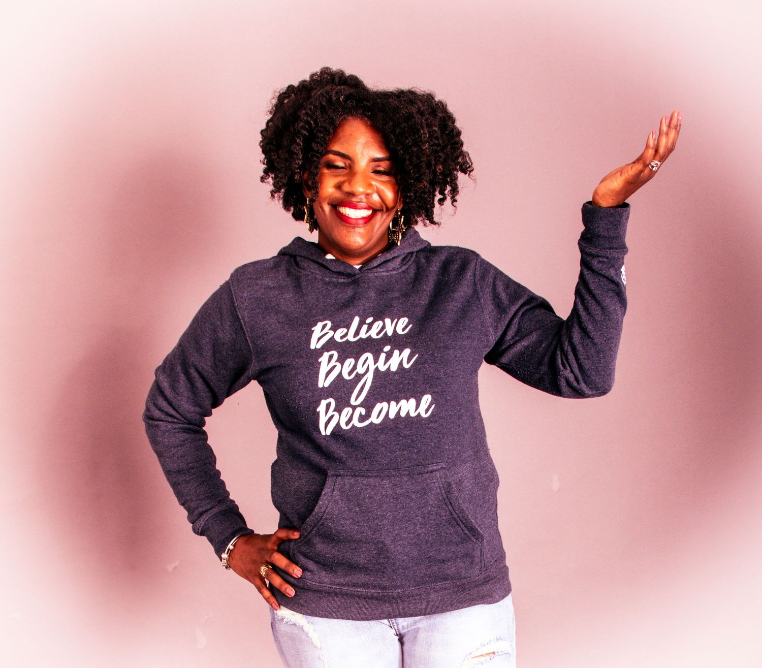 Person wearing a navy blue sweatshirt with inspirational text poses in multiple shots against a pink background.