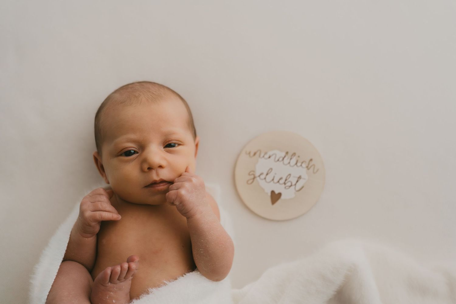 A newborn baby lying on white fabric next to a small decorative circular plaque.