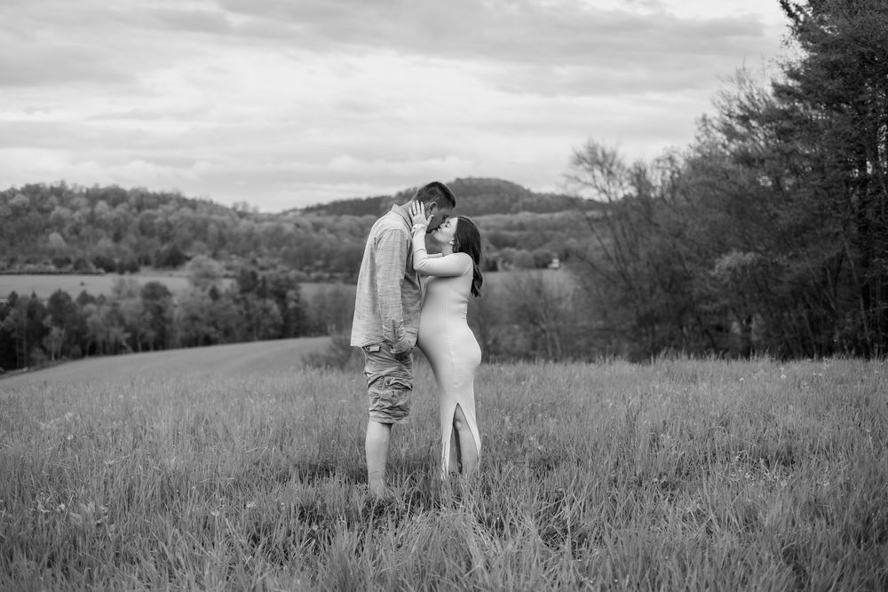 A couple poses in a scenic mountain field during their black and white maternity session.