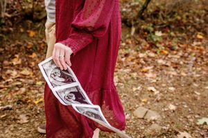 A person in a burgundy dress holds ultrasound photos against an autumn background.