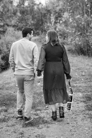 A couple walks away from camera holding ultrasound photos on an autumn trail.