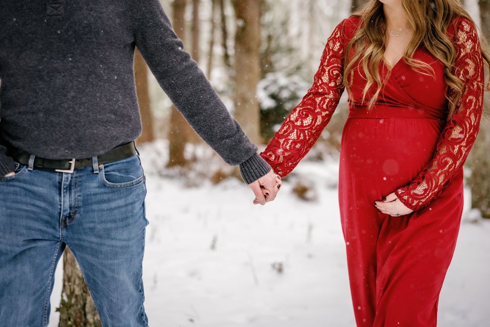 Close-up of holding hands in winter, with red lace dress against snowy forest background.