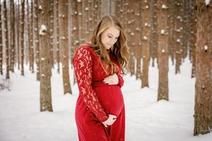 Person in a flowing red lace dress poses in a snowy winter forest setting.