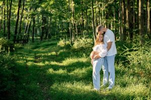 A couple poses in a sunlit forest clearing during their maternity photoshoot.