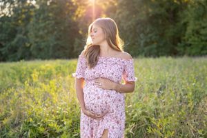 A couple stands in a golden meadow at sunset during their maternity session.
