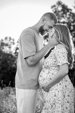 A romantic black and white maternity photo of a couple sharing an intimate moment in a meadow.