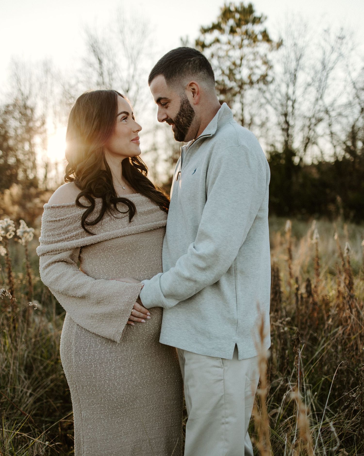 A pregnant woman in a white off-shoulder dress poses in a field during a maternity photoshoot.