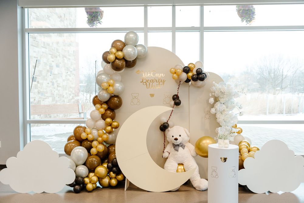 Elegant gold and white baby shower backdrop with moon, teddy bear, balloons, and cloud decorations.