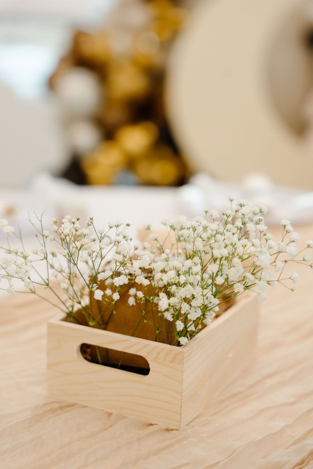 Small wooden crate filled with delicate white baby's breath flowers on a wooden table surface.