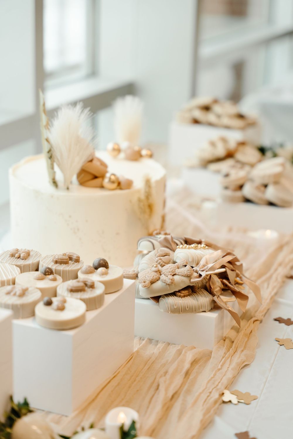 Elegant white and gold baby shower dessert table with tiered cake, macarons, and decorated treats.