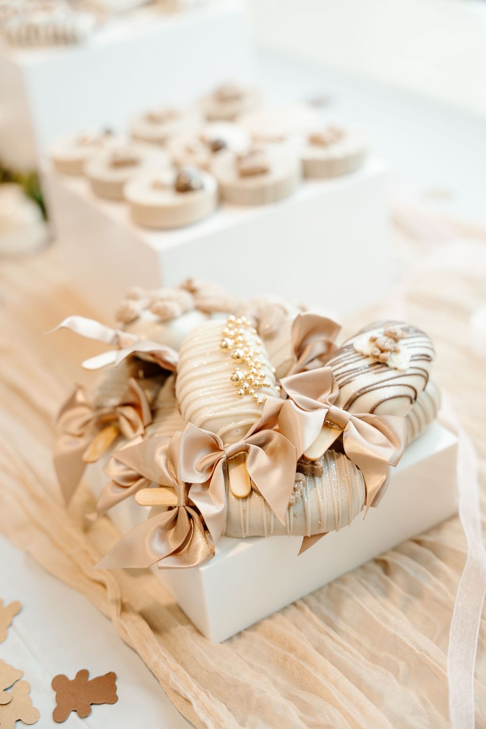 Luxurious beige and gold chocolate-dipped strawberries with satin bows displayed on a white gift box.