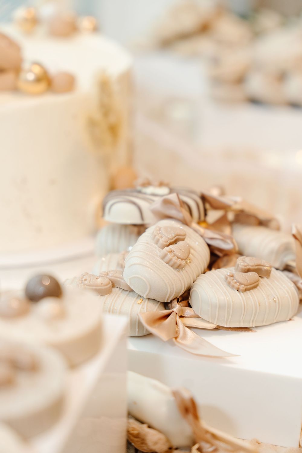 Elegant white and gold baby shower dessert table featuring fondant baby booties and decorated mini cakes.