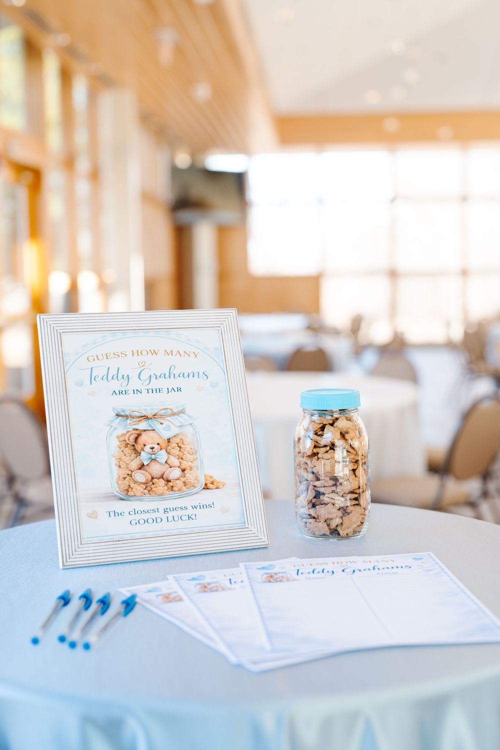 Close-up of a guess how many teddy grahams baby shower game with jar and entry cards on table.