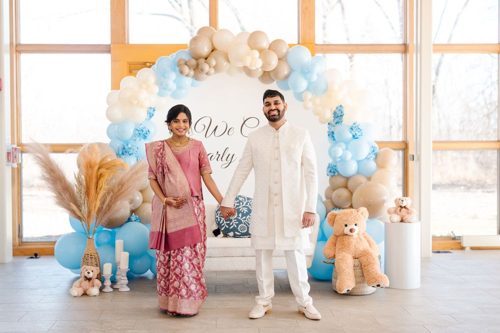 Indian couple in traditional clothing posing at a teddy bear themed baby shower balloon backdrop.