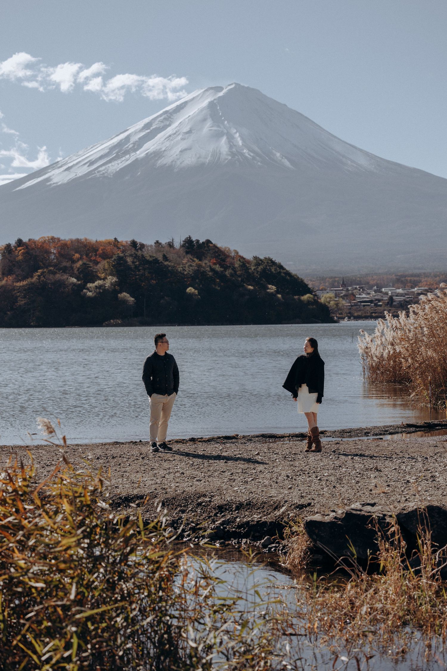 Mount Fuji rises majestically over Lake Kawaguchiko with autumn reeds and shoreline in the foreground.