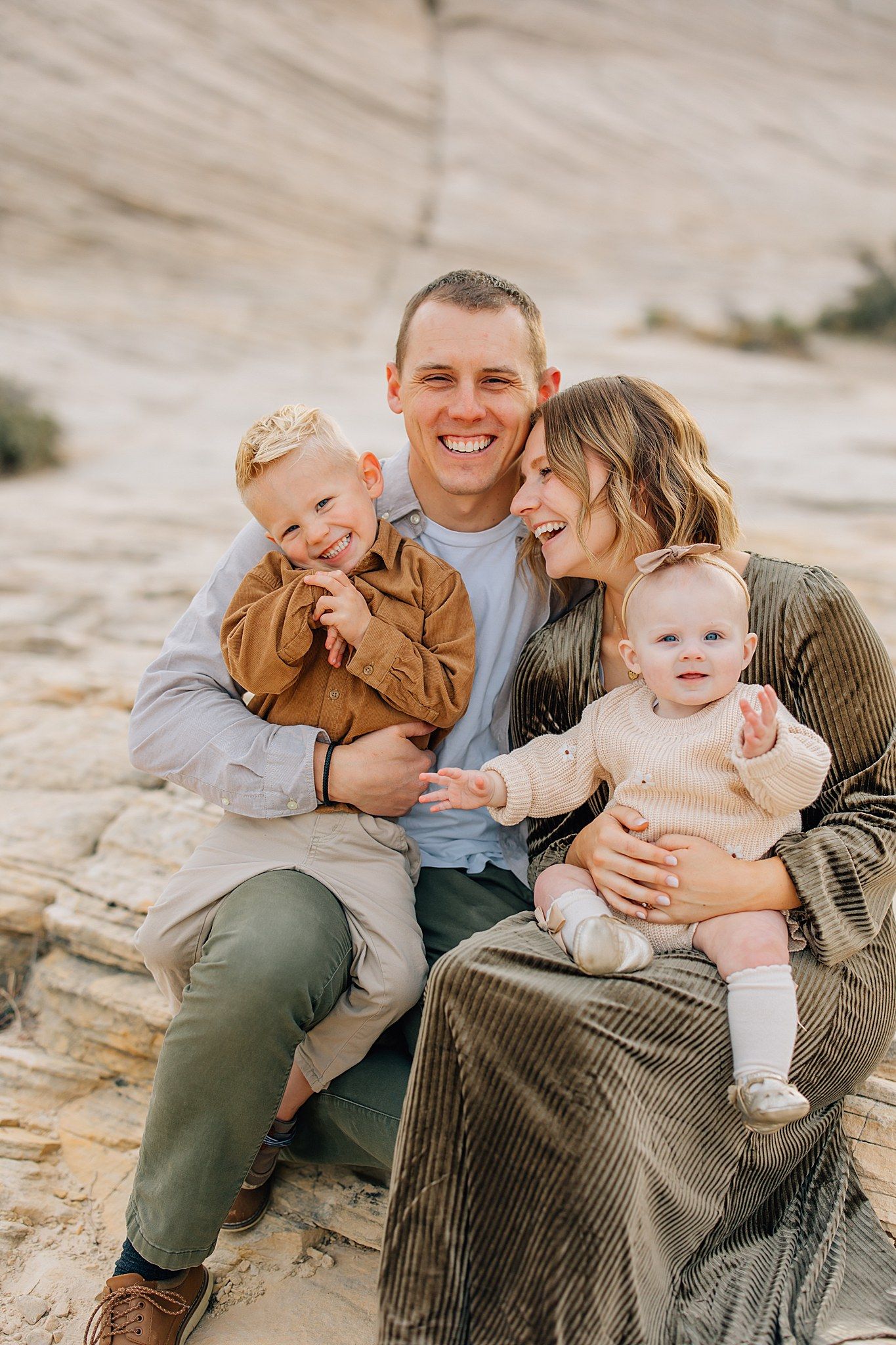 A family sits together on rocky terrain wearing earth-toned clothing while sharing intimate candid moments.