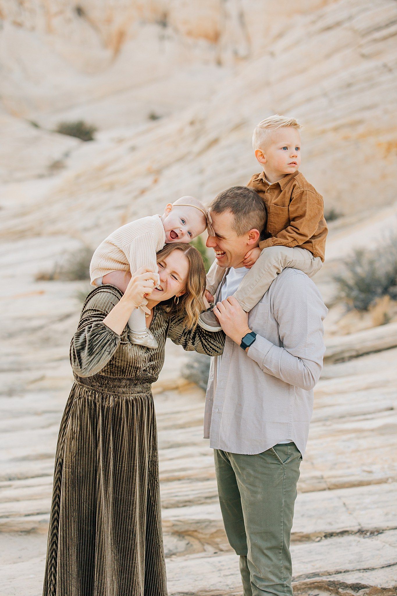 A couple shares a playful moment in front of a rocky desert landscape while wearing casual fall attire.
