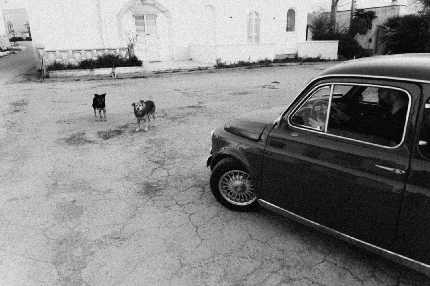 A black vintage car is parked on a dirt road in a black and white photograph.