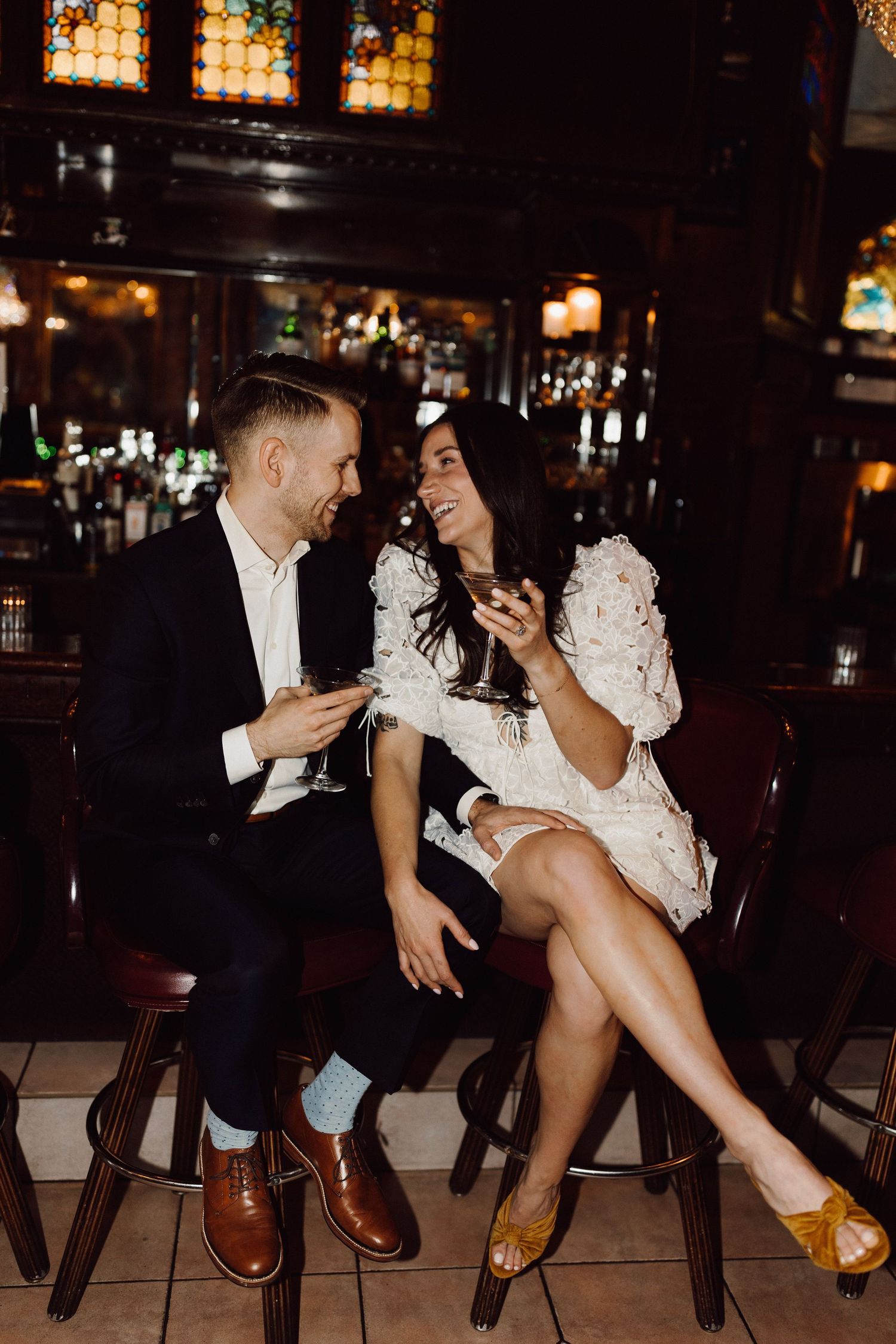 Couple sitting on wooden chairs in a dimly lit bar sharing an intimate moment.