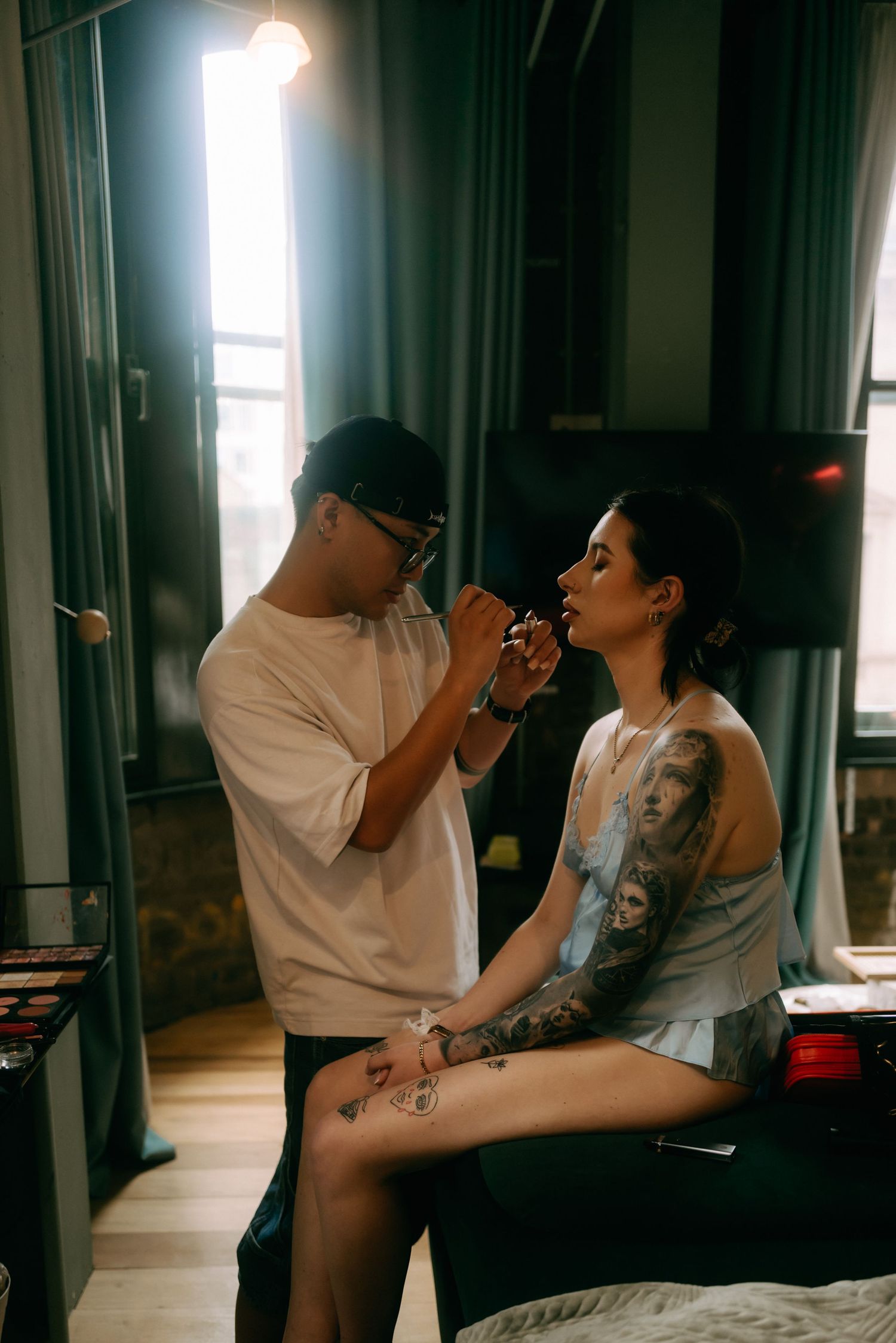 Two people share intimate moments while smoking in a dimly lit room with window light.