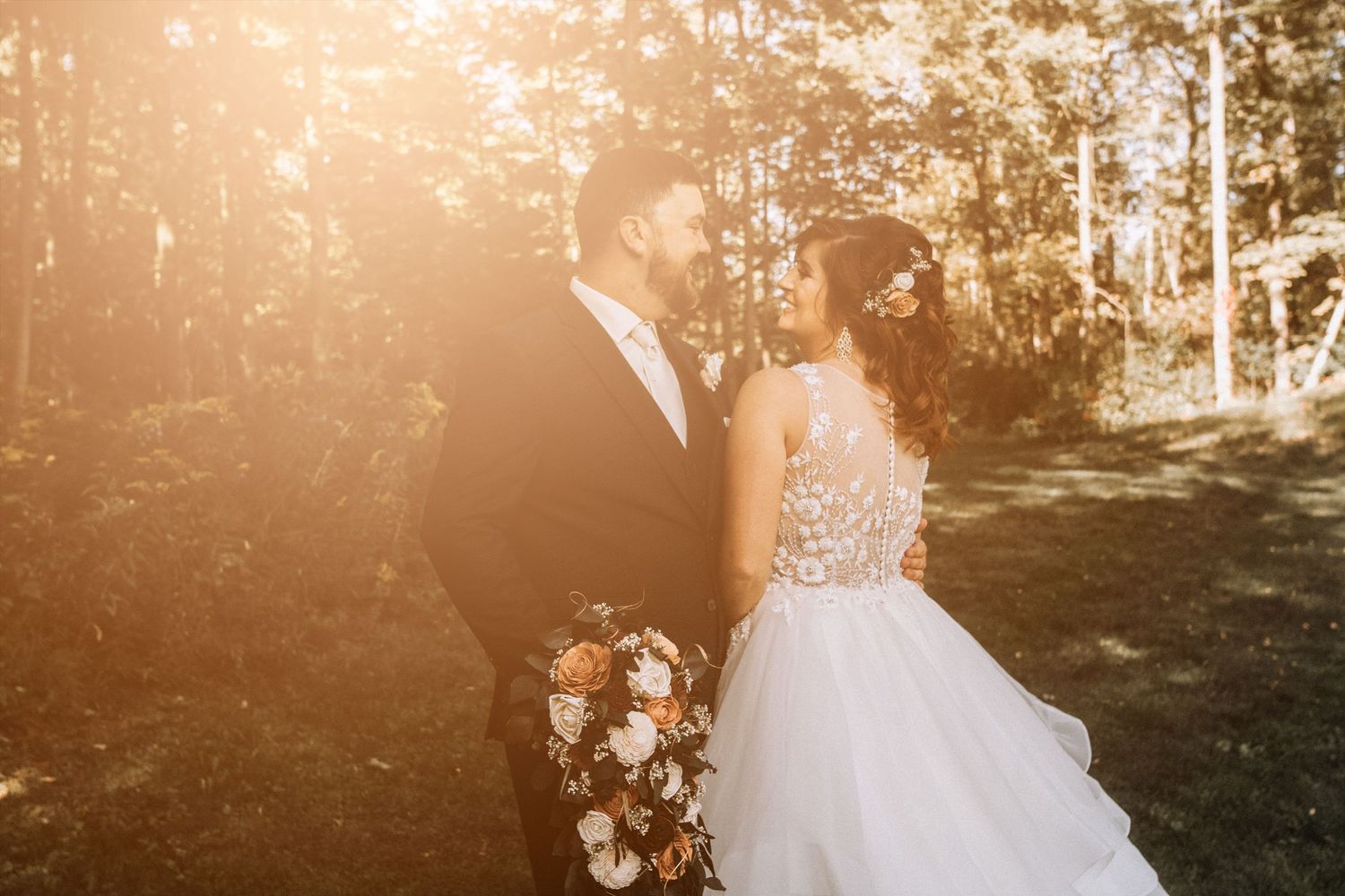 A romantic wedding couple walks through a sunlit forest path while holding hands during golden hour.