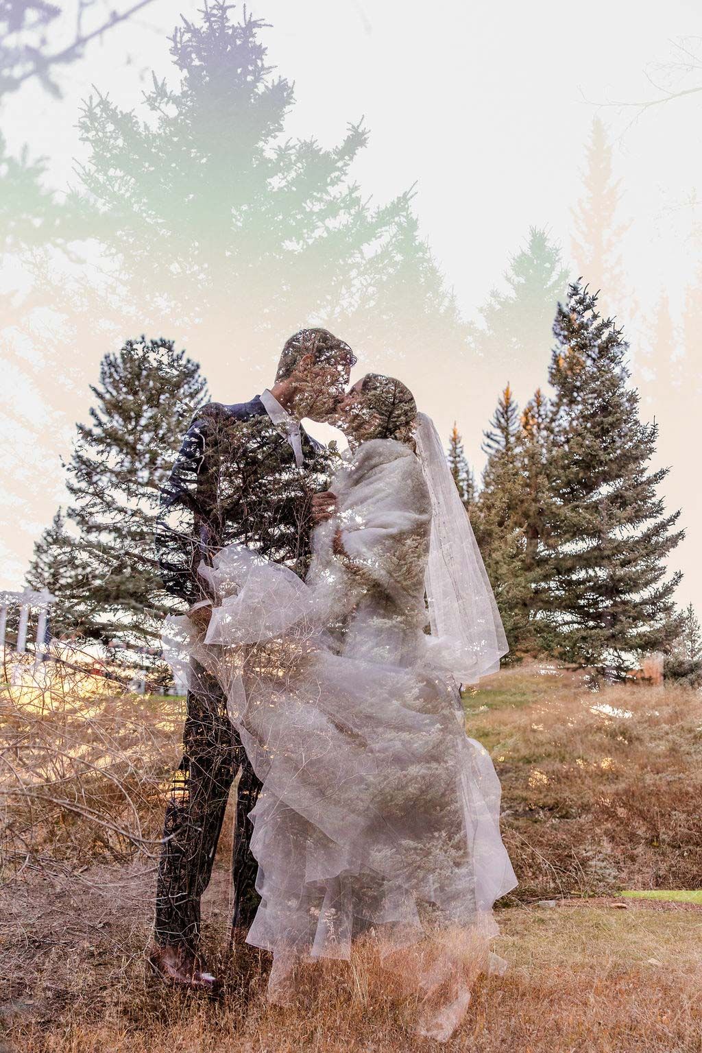 A couple poses together in a field at sunset with flowing white tulle fabric creating an ethereal effect.