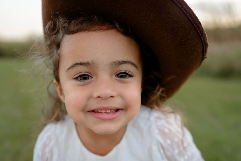 A young child with curly brown hair smiles while playing outdoors in natural lighting.