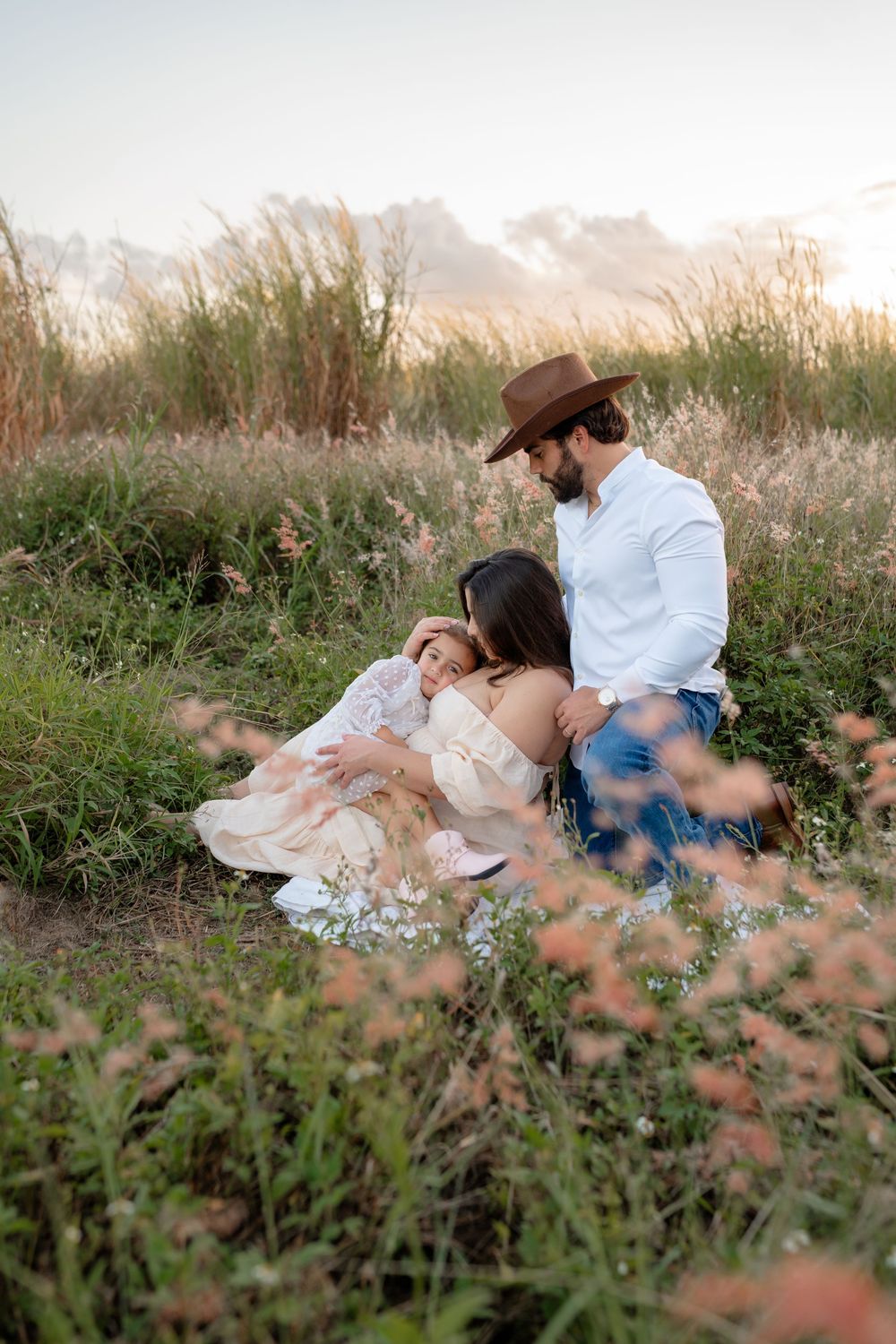 Family lying together on a blanket in a grassy field during golden hour sunset.