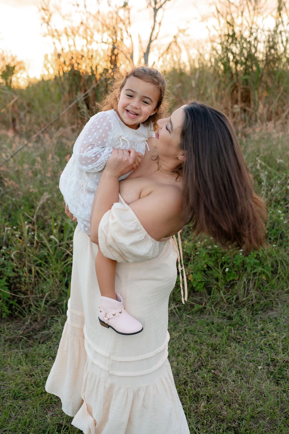 Joyful mother and child playing together outdoors in white dresses.