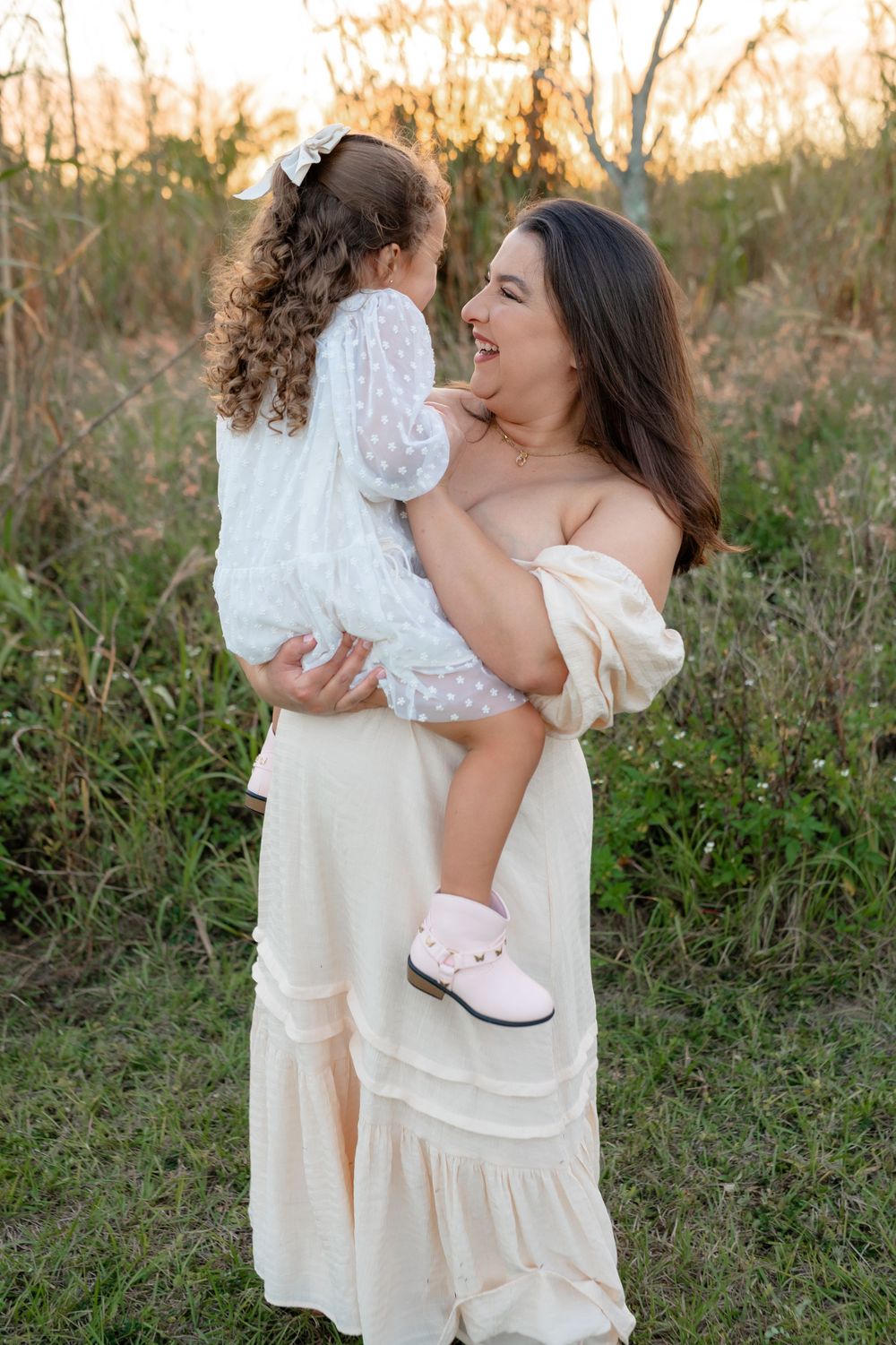 Mother and daughter in white dresses embracing outdoors at sunset.