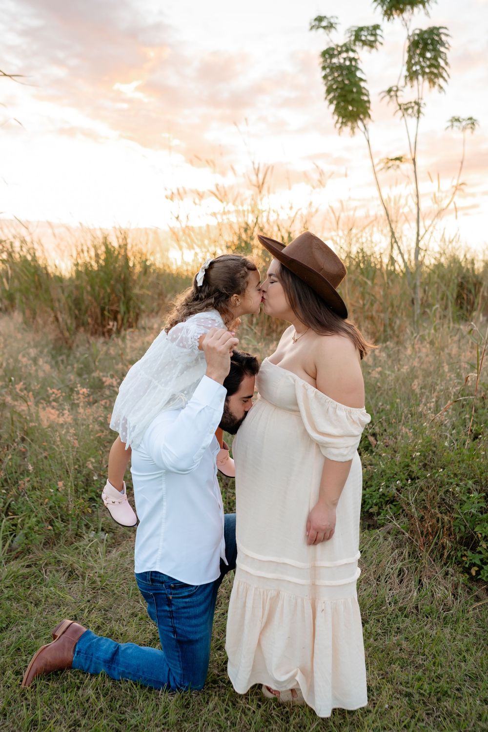 Playful family moment in a field during sunset wearing coordinated white and denim outfits.