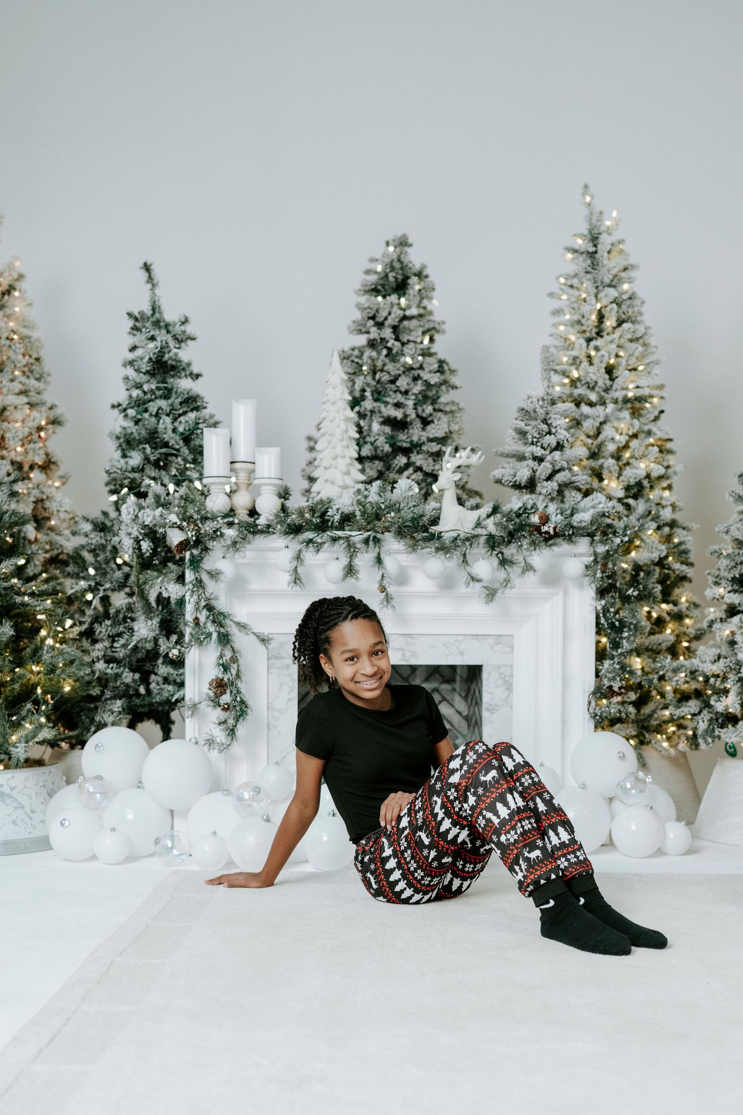A festive holiday photo shoot with decorated Christmas trees and white decor in a cozy studio setting.