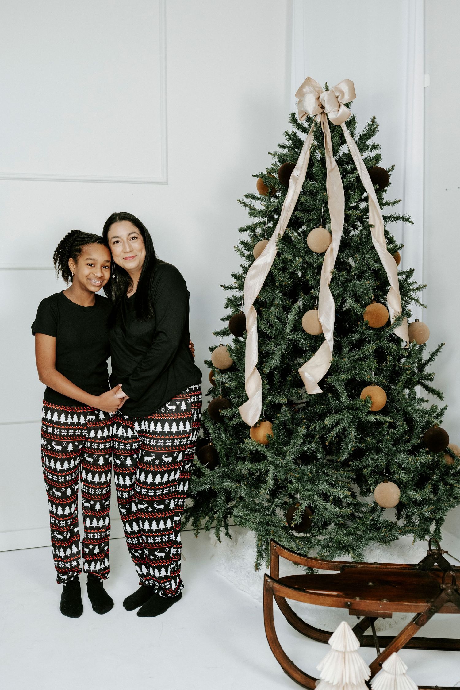 A playful holiday photoshoot featuring matching festive pajama pants and decorated Christmas trees in a bright studio.