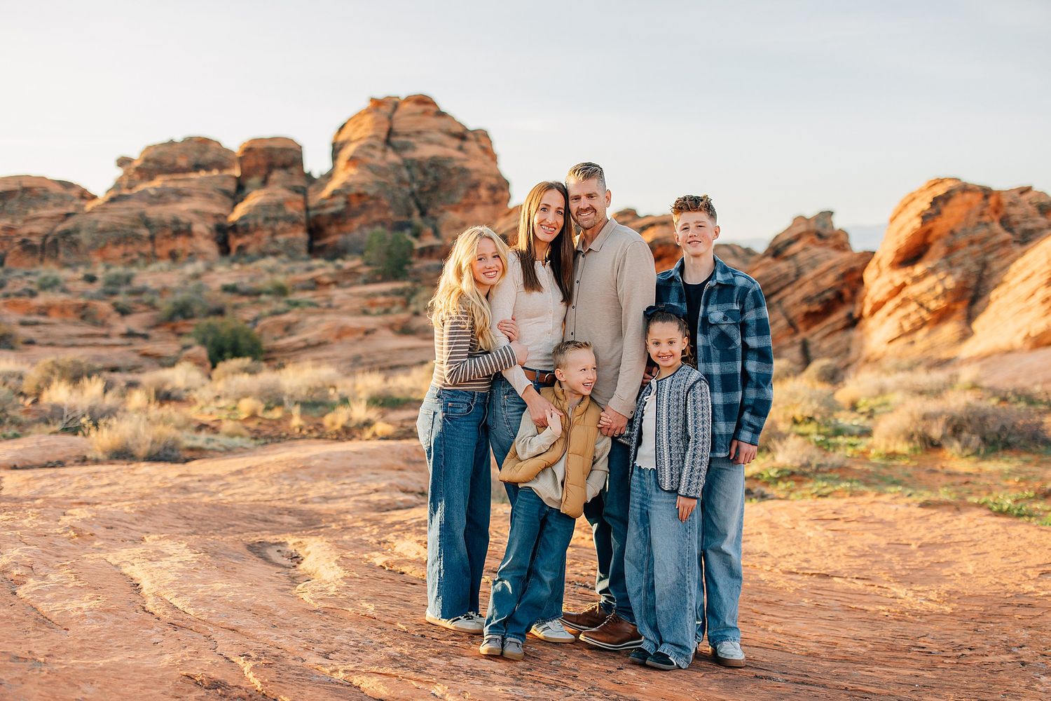 A group poses together on red rock formations in Arches National Park at sunset.