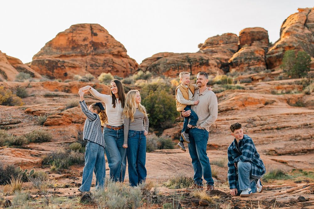 Family walking together on scenic red rock formations in desert landscape during golden hour.