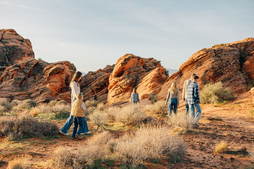 A group of people hiking through scenic red rock formations in a desert landscape during golden hour.