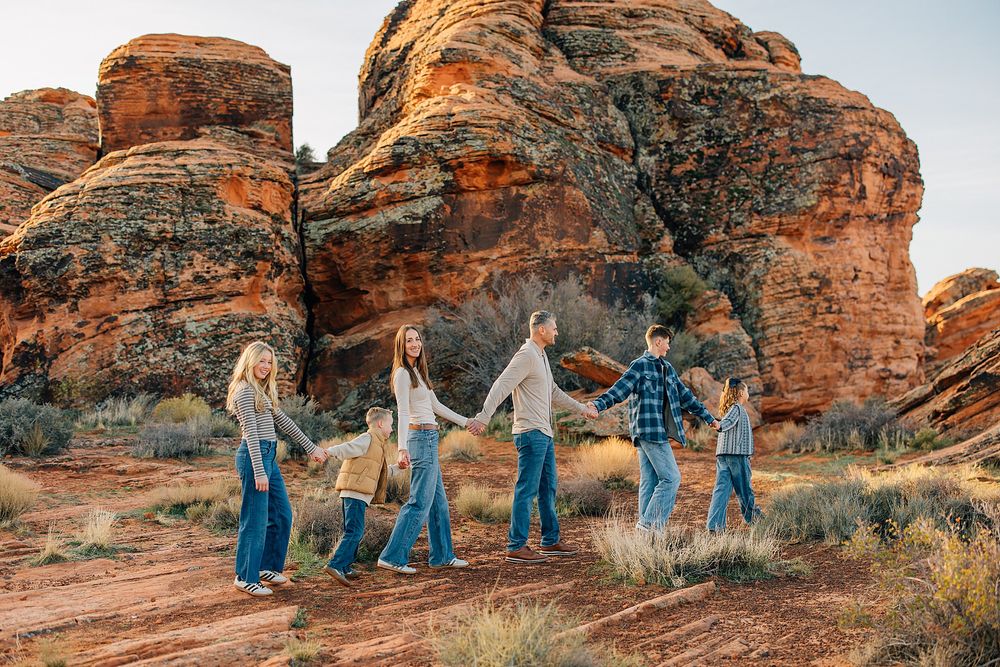 People in coordinating blue outfits walk through red rock formations in a desert landscape at sunset.