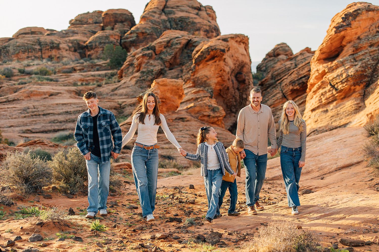 A group walks together along scenic red rock formations in a desert landscape during golden hour lighting.
